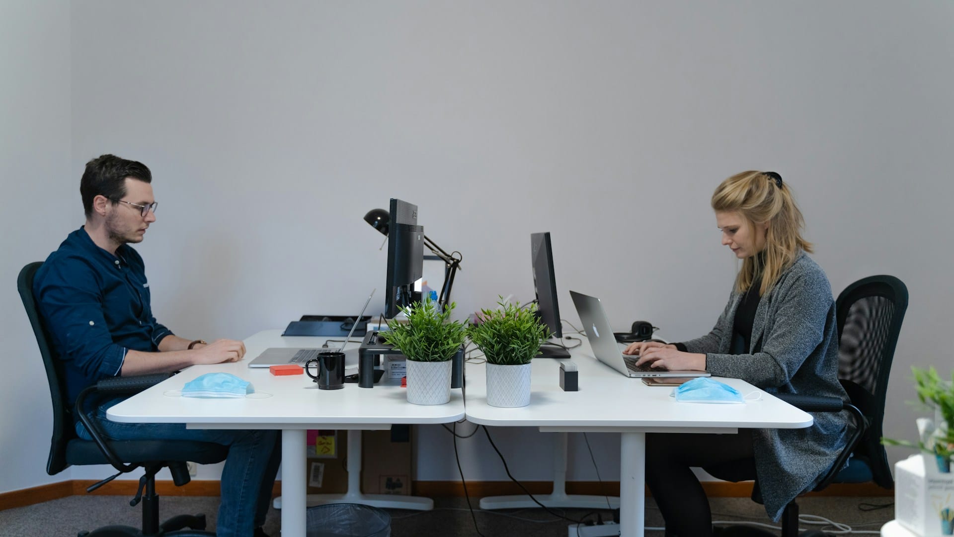 Man and woman working at separate desks on laptops and monitors in a minimalist office
